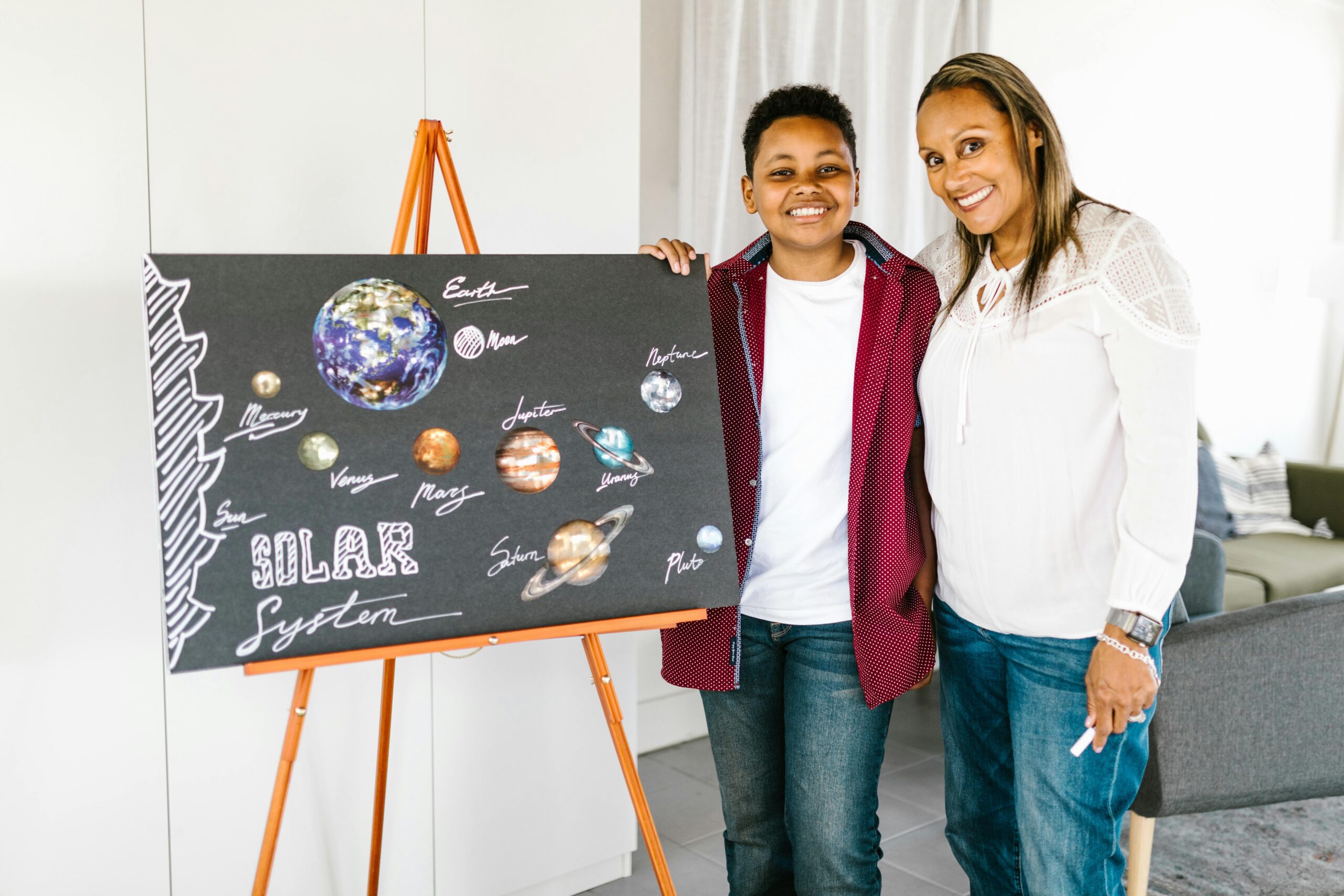 Mother and son standing next to displayed poster board about planets